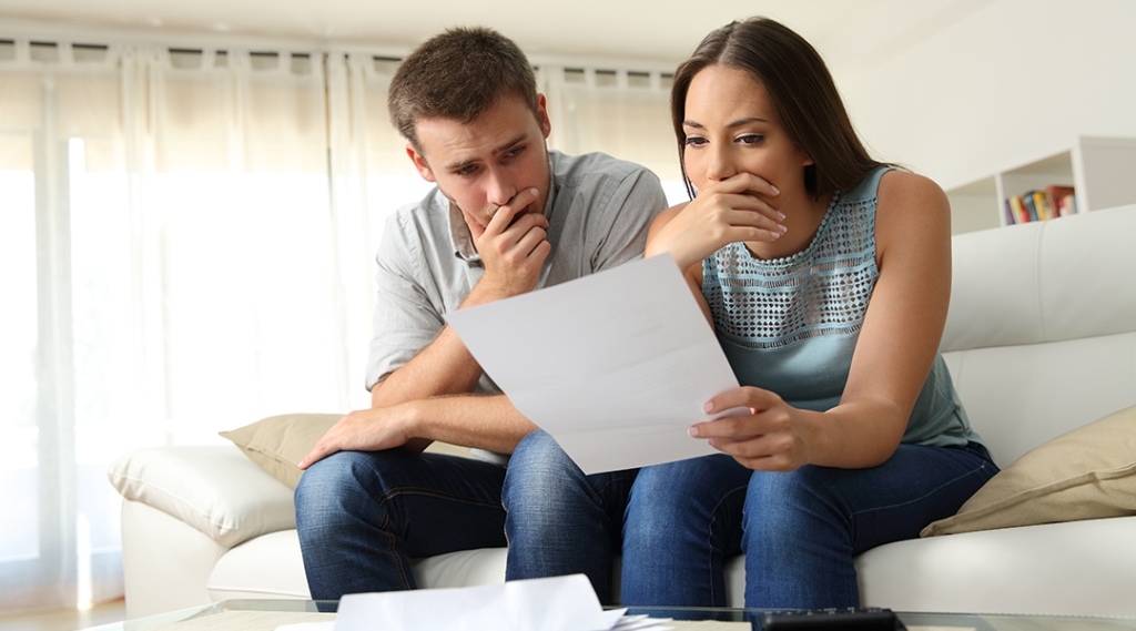 Un homme et une femme assis sur un canapé, regardant un morceau de papier
