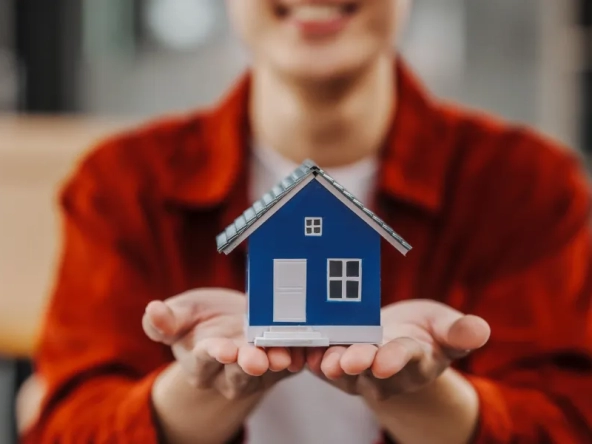 Une personne tenant un modèle de maison dans ses mains, symbolisant la valeur de votre maison.